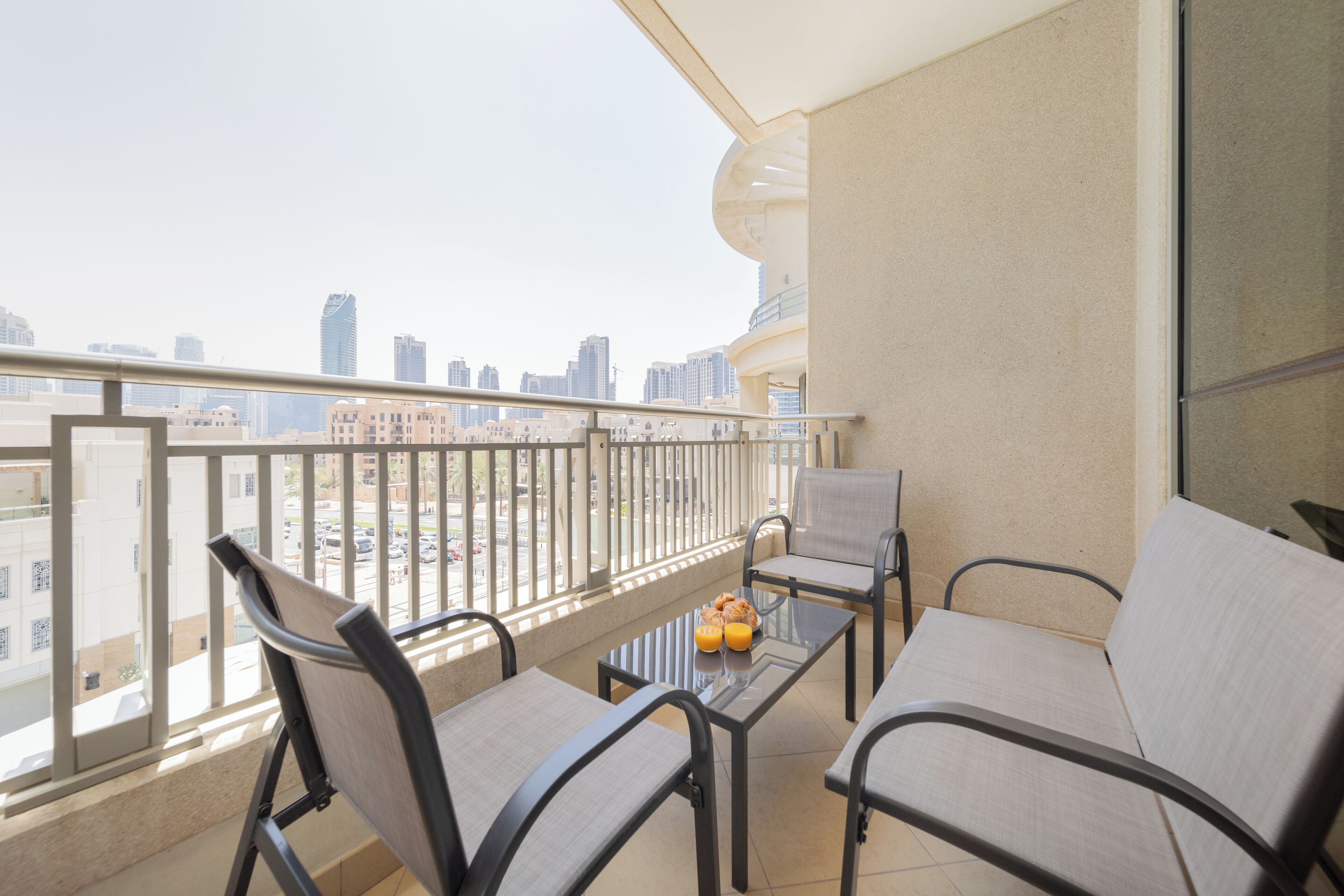 A balcony with two chairs and a table, a glass partition, and a city view.