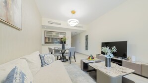 A modern living room with a sofa, coffee table, TV, and a dining area with chairs and a table.