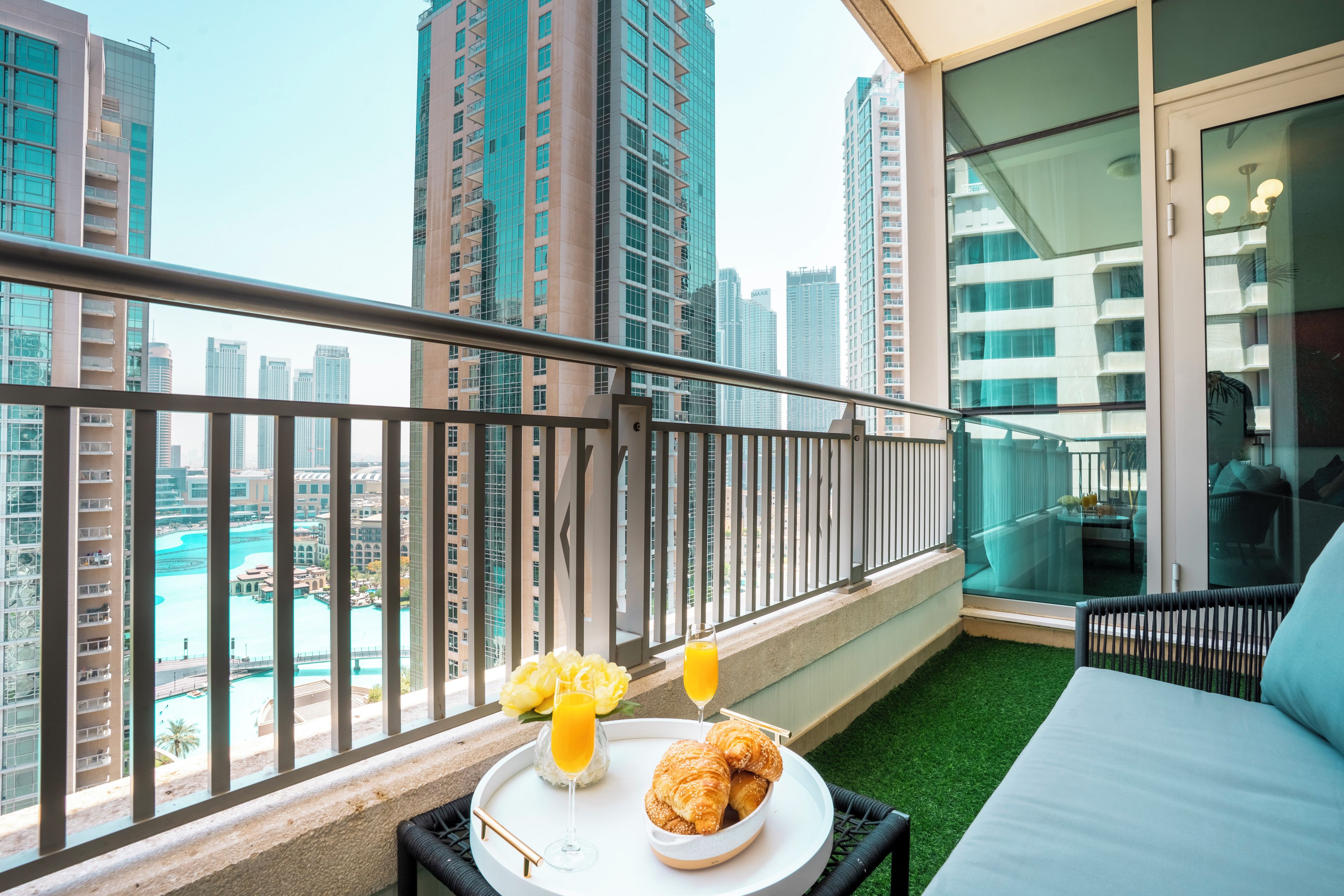 Een balkon met uitzicht op een stadsgezicht, een bed, een tafel met croissants en sap, en een glas sinaasappelsap.