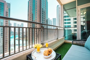 Ein Balkon mit Blick auf eine Stadtlandschaft, ein Bett, ein Tisch mit Croissants und Saft sowie ein Glas Orangensaft.