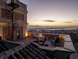 Una terrazza sul tetto con una scala a chiocciola, un'amaca e vista sulla città e sul fiume al tramonto.