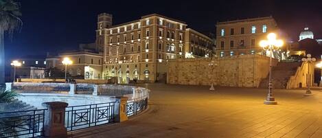 Ein historisches Gebäude mit klassischer Architektur, einer Fontäne und einem gut beleuchteten Platz bei Nacht.
