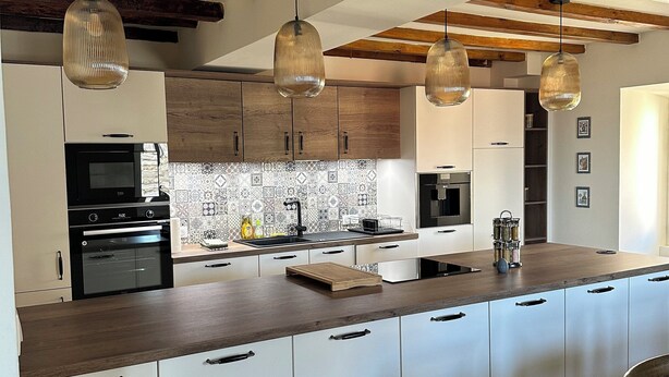 A modern kitchen with a large island, wooden beams on the ceiling, and pendant lighting. - Charming air-conditioned house with garden and view on the Propriano bay (Olmeto)