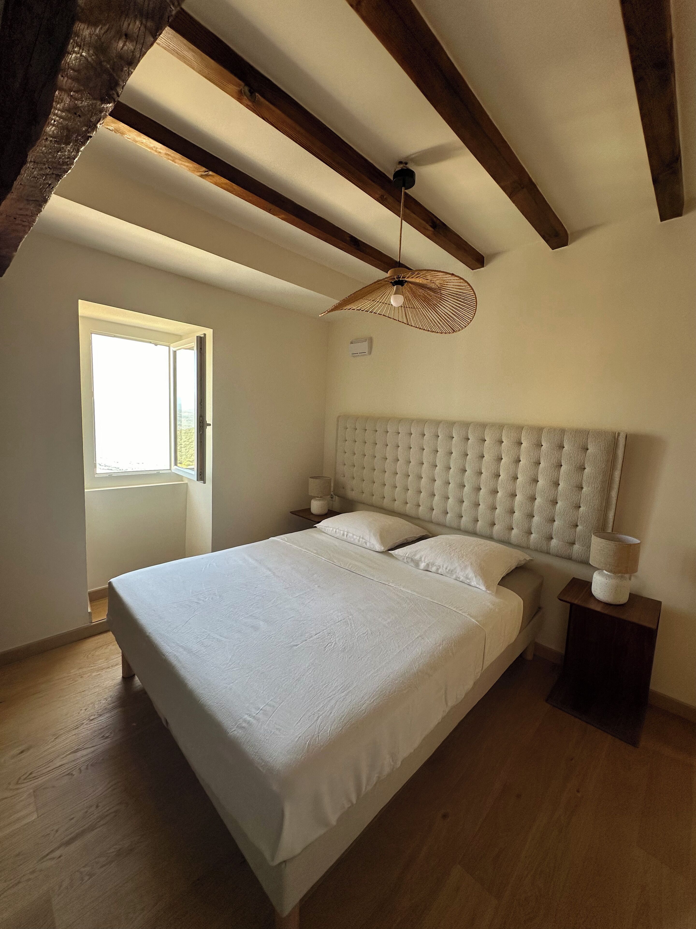 Un dormitorio con una cama grande, vigas de madera, un ventanal y una lámpara colgante.