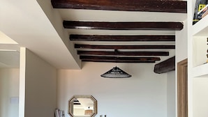 A room with exposed wooden beams, a fireplace, a grey sofa, and a hanging light fixture. - Charming air-conditioned house with garden and view on the Propriano bay (Olmeto)
