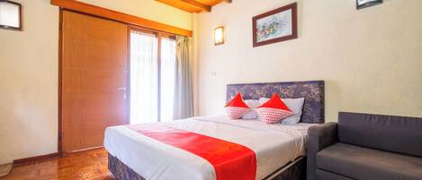 A bedroom with a wooden floor, a bed with a red blanket, a grey sofa, and a wooden ceiling.