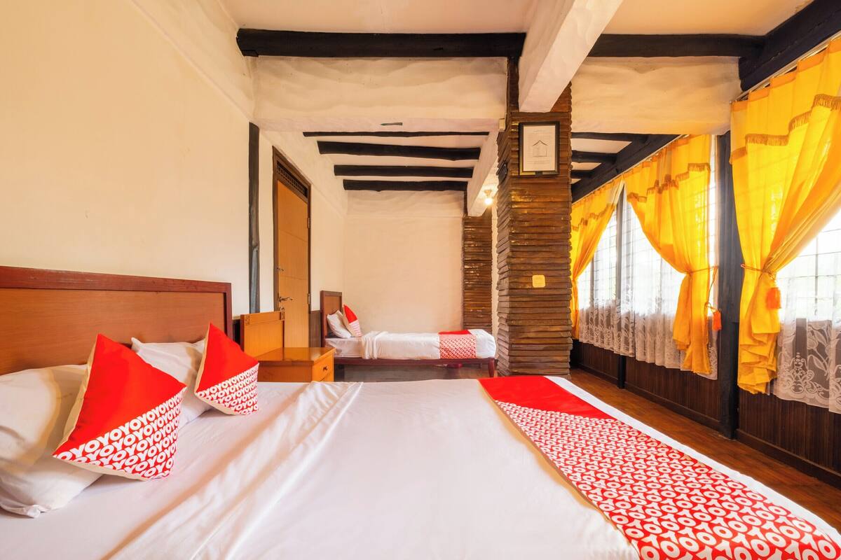 Una habitación de hotel con una cama grande, dos almohadas, un cabecero de madera, una mesita de noche, una pared de madera y una ventana con cortinas.