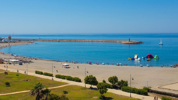 Une plage avec une jetée, une eau d’un bleu limpide et des gens qui profitent des lieux.