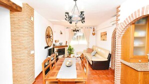 Un coin repas avec une table en bois, des chaises, un lustre et une cheminée en briques.