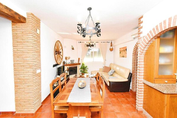Un coin repas avec une table en bois, des chaises, un lustre et une cheminée en briques.