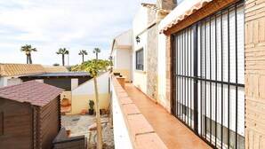 Une ruelle étroite, avec un bâtiment en briques sur la droite, une petite construction en bois sur la gauche et une rangée de palmiers en arrière-plan.