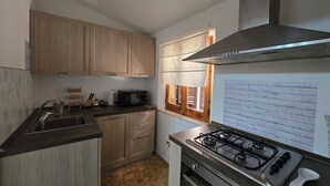 A compact kitchen with wooden cabinets, a gas stove, a microwave, and a window with blinds.
