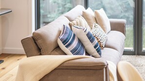 A modern living room with a sofa, pillows, and a large window. - StayAU Stylish 4BR Home Ringwood (Ringwood East)