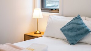 A neatly made bed with a blue pillow, a folded towel, and a lamp on a bedside table. - StayAU Stylish 4BR Home Ringwood (Ringwood East)