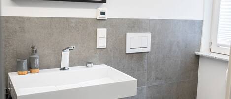 Un baño moderno con un lavamanos blanco, un inodoro y un espejo.