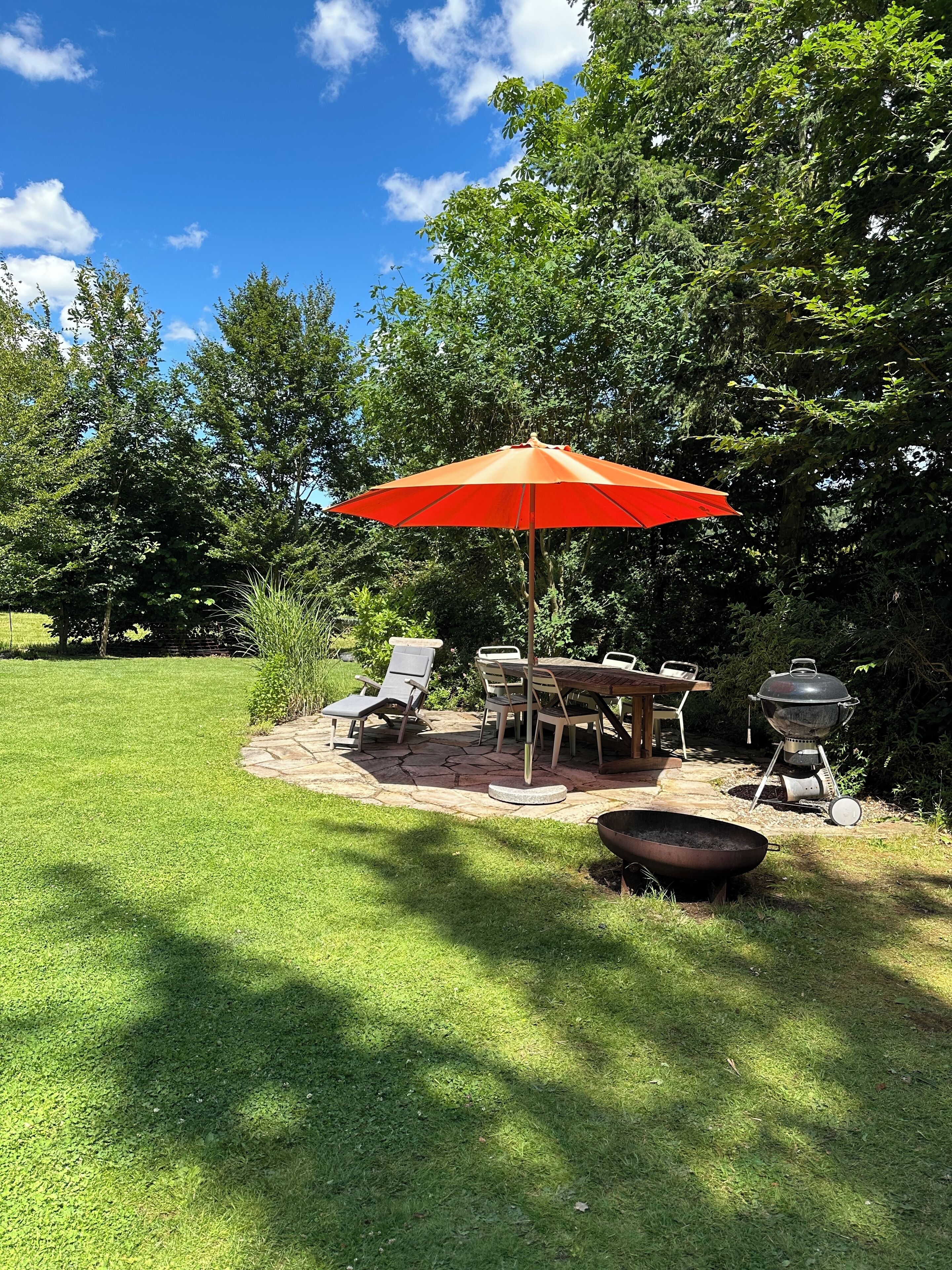 An outdoor patio with a table and chairs, a barbecue grill, and a large umbrella.