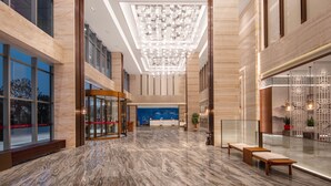 A spacious lobby with a marble floor, a reception desk, and a modern chandelier. - Jiangshan Haiwaihai Hotel (Quzhou)