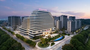 A modern hotel with a multi-story structure, surrounded by other buildings and greenery. - Jiangshan Haiwaihai Hotel (Quzhou)