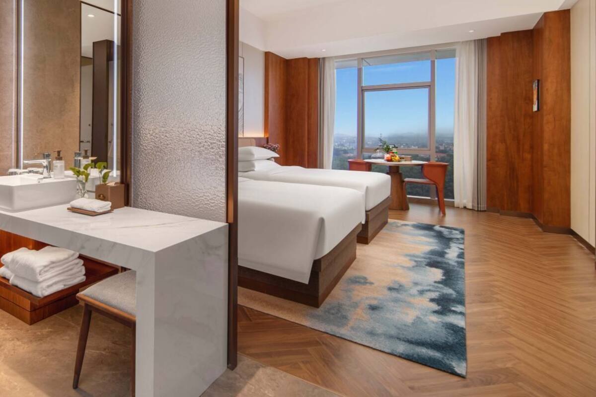 A modern hotel room with a large bed, a desk with a mirror, a bathroom with a sink, and a view of the city.