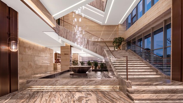 A modern interior with a marble staircase, a central water feature, and a high ceiling with geometric lighting. - Jiangshan Haiwaihai Hotel (Quzhou)