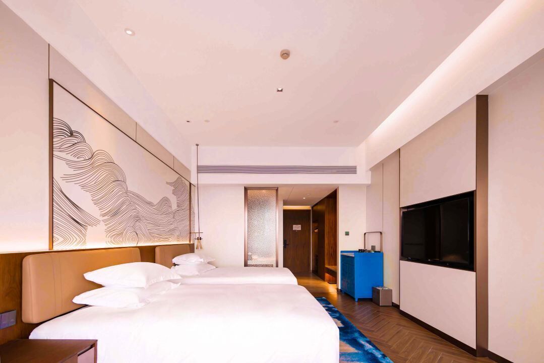 A hotel room with a large bed, a TV, a desk, and a decorative wall piece.