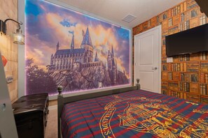 Ein Schlafzimmer mit großem Wandgemälde eines Schlosses, einem Bett mit passender Bettdecke, einem Bücherregal und einem an der Wand befestigten Fernseher.