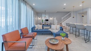 A modern living room with a sofa, chairs, a coffee table, and a staircase leading to an upper level. - Stylish 5BR Retreat with Pool Near Disney (Davenport)