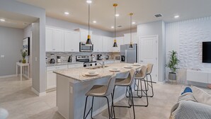 A modern kitchen with white cabinets, a large island with bar stools, and stainless steel appliances. - Stylish 5BR Retreat with Pool Near Disney (Davenport)