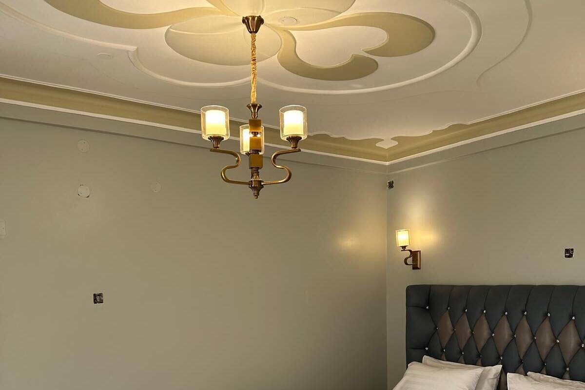 A bedroom with a tufted headboard, a large bed, a chandelier, and wall sconces.
