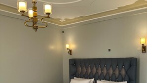 Une chambre à coucher avec une tête de lit capitonnée, un grand lit avec du linge de lit blanc, un lustre et des appliques murales.