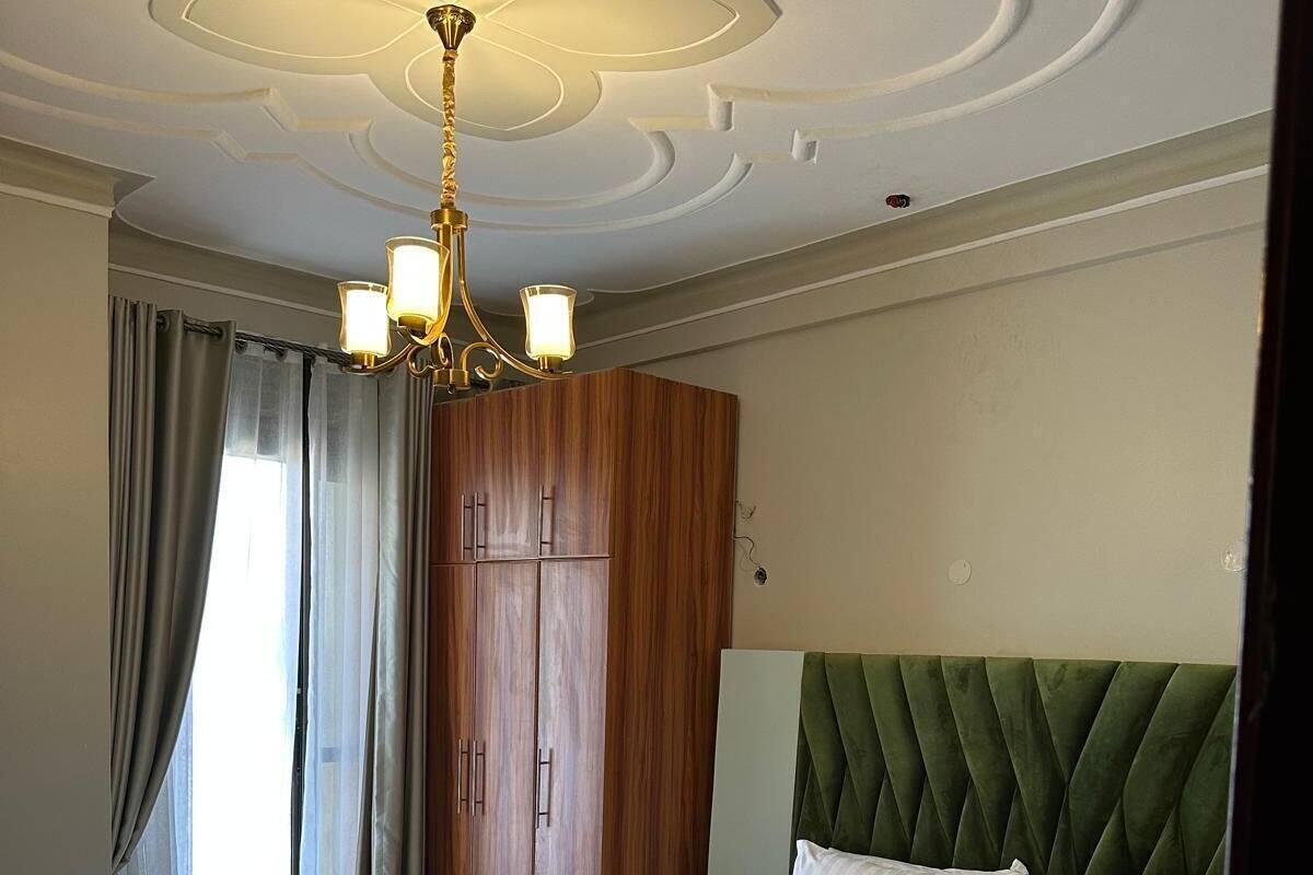 A hotel room with a large bed, a green upholstered headboard, a wooden wardrobe, and a chandelier.