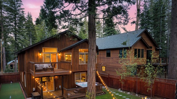 A two-story wooden cabin with a deck, outdoor seating, and a fire pit.