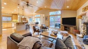A spacious living room with a wooden ceiling, a stone fireplace, and a large TV.