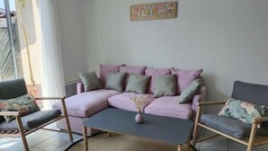 Ett vardagsrum med en rosa soffa, två fåtöljer, ett soffbord och en skylt med texten ”GLAD” på väggen.