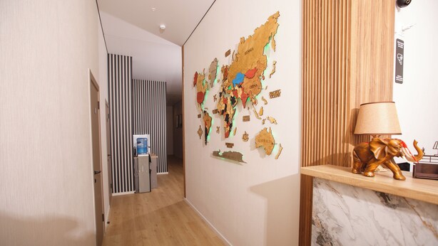 A hallway with a wooden floor, a world map on the wall, a reception desk with a lamp, and a striped partition. - ASYL HOTEL (Astana)