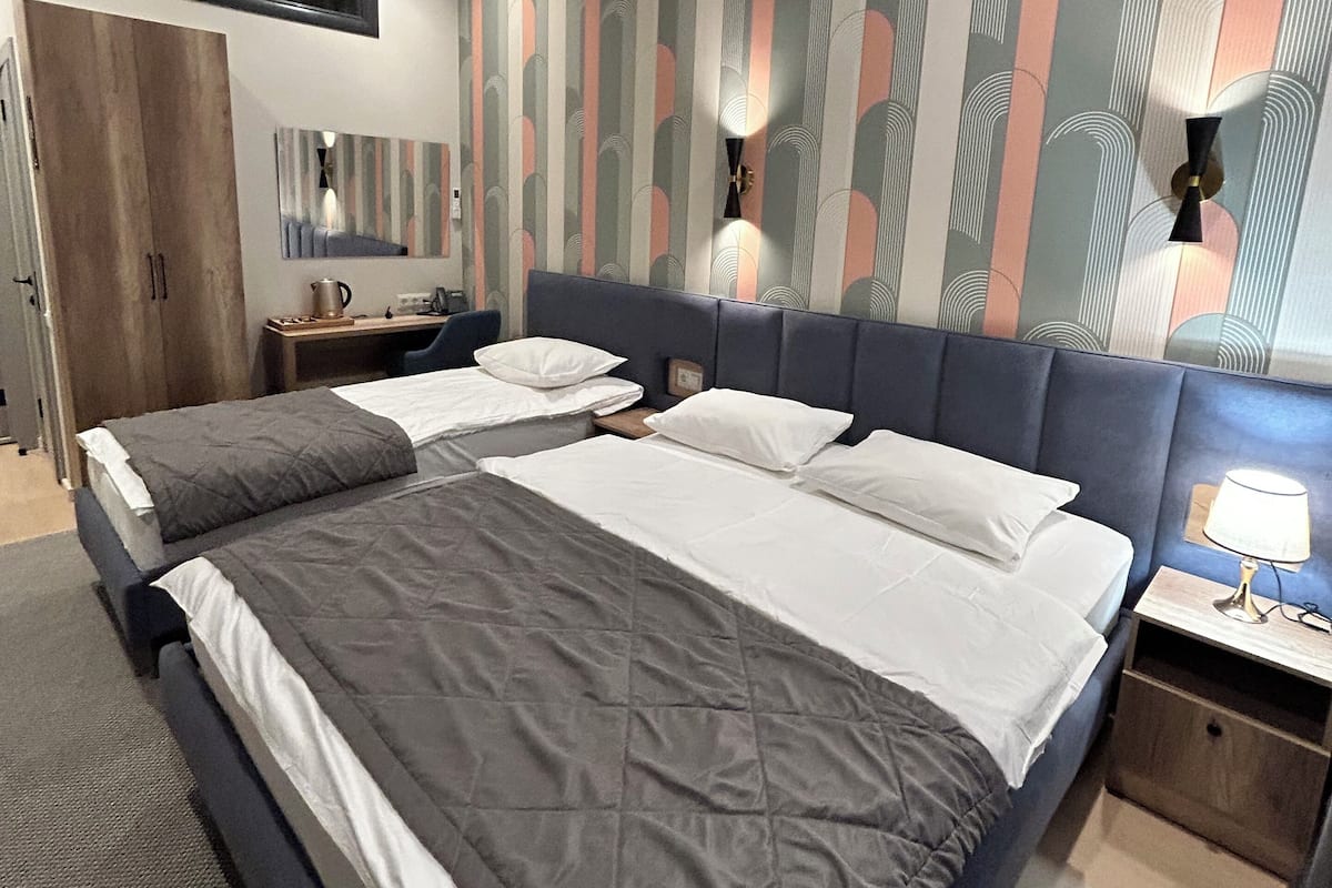 A hotel room with two beds, a wardrobe, a mirror, a wall-mounted TV, and an air conditioning unit.