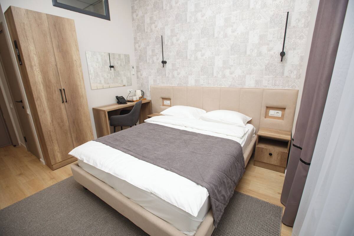 A modern bedroom with a large bed, a desk, and a wardrobe.