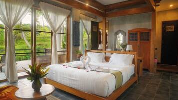 A spacious bedroom with a large bed, a small table with a plant, and a view of greenery outside.