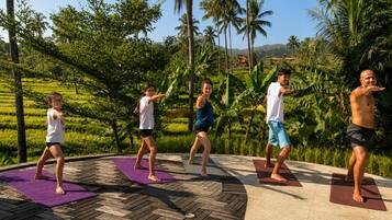 Un grupo de personas practicando yoga al aire libre sobre una terraza de madera, con abundante follaje y palmeras de fondo.