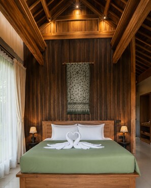 A wooden-paneled bedroom with a bed, two bedside lamps, and a hanging tapestry. - Villa OMantra Home Bali (Sukasada)