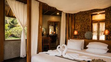 Una habitación con una cama, cortinas blancas, techo de madera, un espejo y vistas a la vegetación exterior.