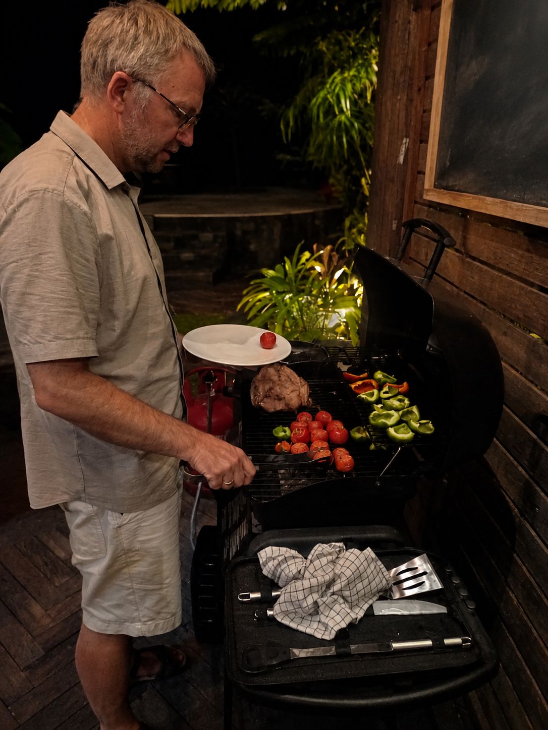Un homme qui fait griller des légumes et de la viande sur un barbecue extérieur.