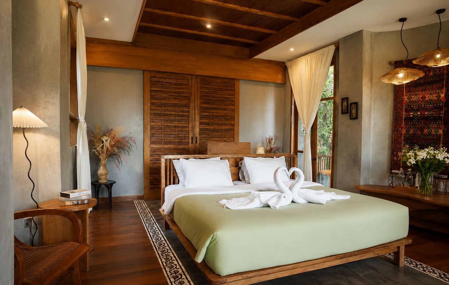A hotel room with a large bed, wooden headboard, and a view of greenery outside.