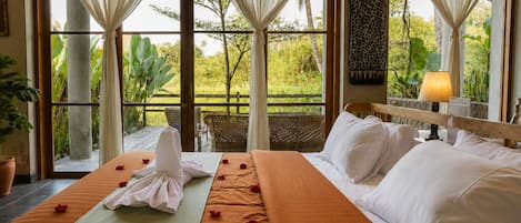 A hotel room with a large bed, a balcony, and a view of greenery.