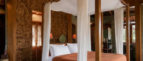 A four-poster canopy bed with white drapes, a stone wall, and a wooden ceiling.