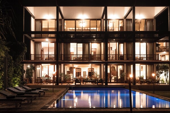 A multi-story hotel with a swimming pool, outdoor seating, and a well-lit facade.