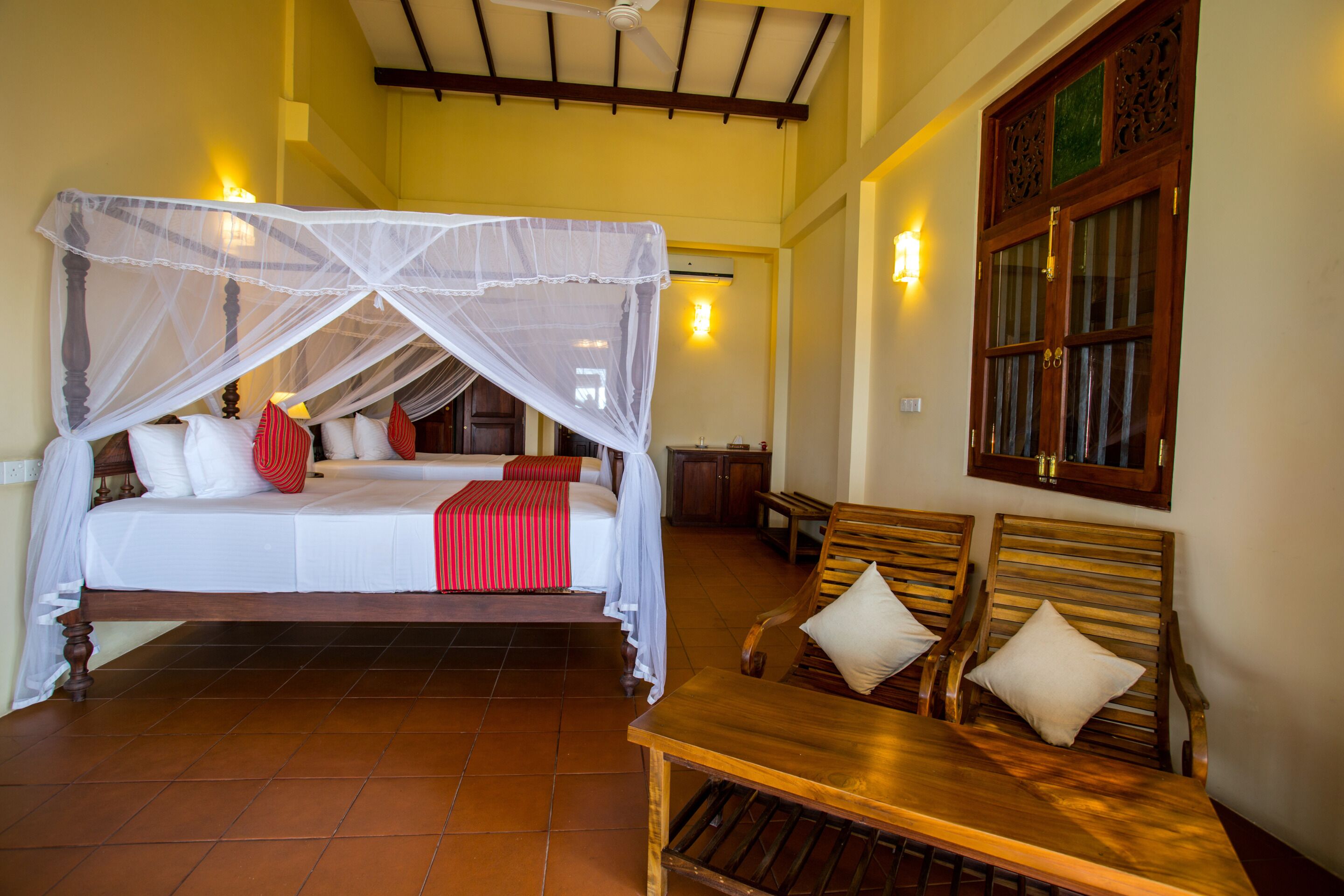 Una habitación con una cama bajo una mosquitera, muebles de madera y una ventana con detalles decorativos.