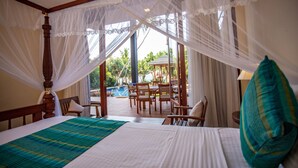 A room with a bed, a wooden chair, a table, and a view of a pool and greenery outside. - South Point Ocean - Whole Villa 8 Bedroom (Sleep 16) (Koggala)