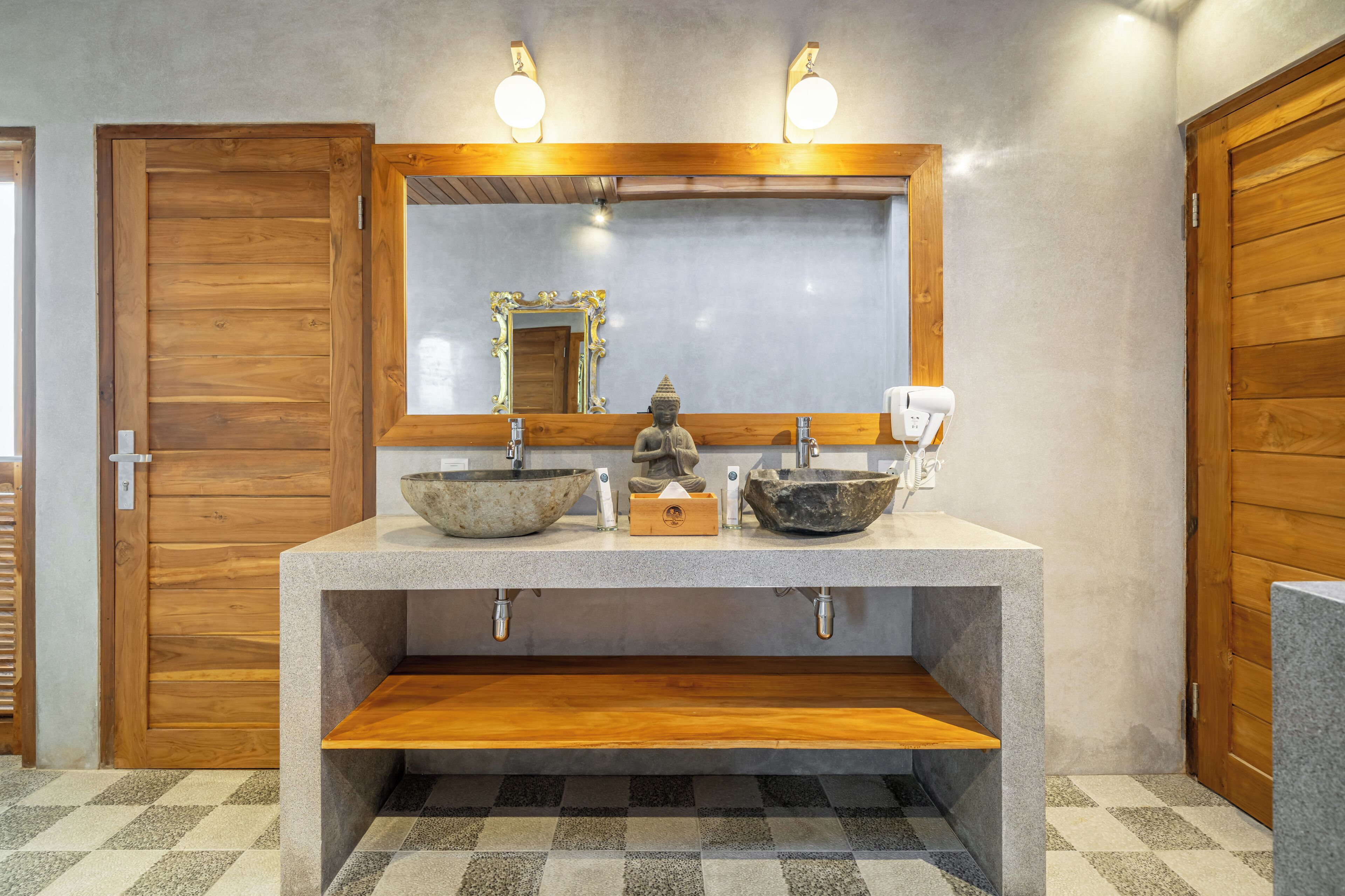 Un bagno con una porta in legno, un lavandino con una bacinella, uno specchio con cornice decorativa e un dispenser di asciugamani.