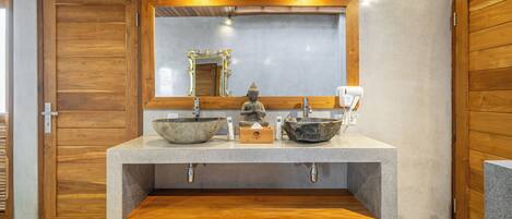 Un bagno con una porta in legno, un lavandino con una bacinella, uno specchio con cornice decorativa e un dispenser di asciugamani.